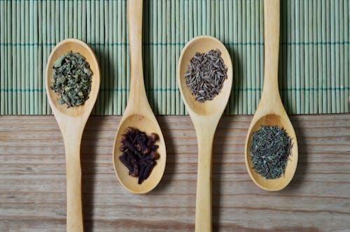 Free Brown Wooden Spoon With Herbs on Top of Green Bamboo Mat and Brown Wooden Surface Stock Photo