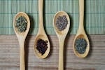 Brown Wooden Spoon With Herbs on Top of Green Bamboo Mat and Brown Wooden Surface