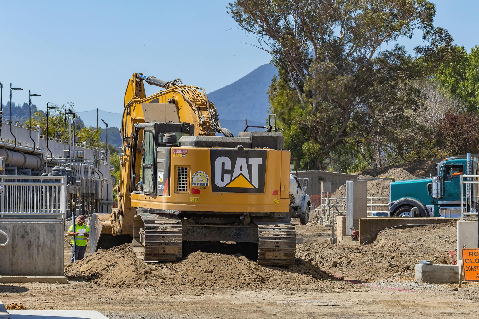 Excavator working at a construction site with mountains in the background.