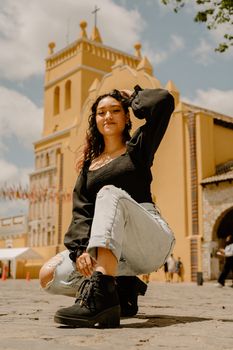Fashionable young woman in denim and boots posing confidently outdoors in front of a church.