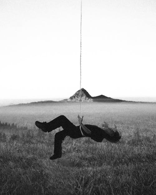 Free Woman Hanging from a Rope above Meadow and Performing Acrobatic Dance Stock Photo