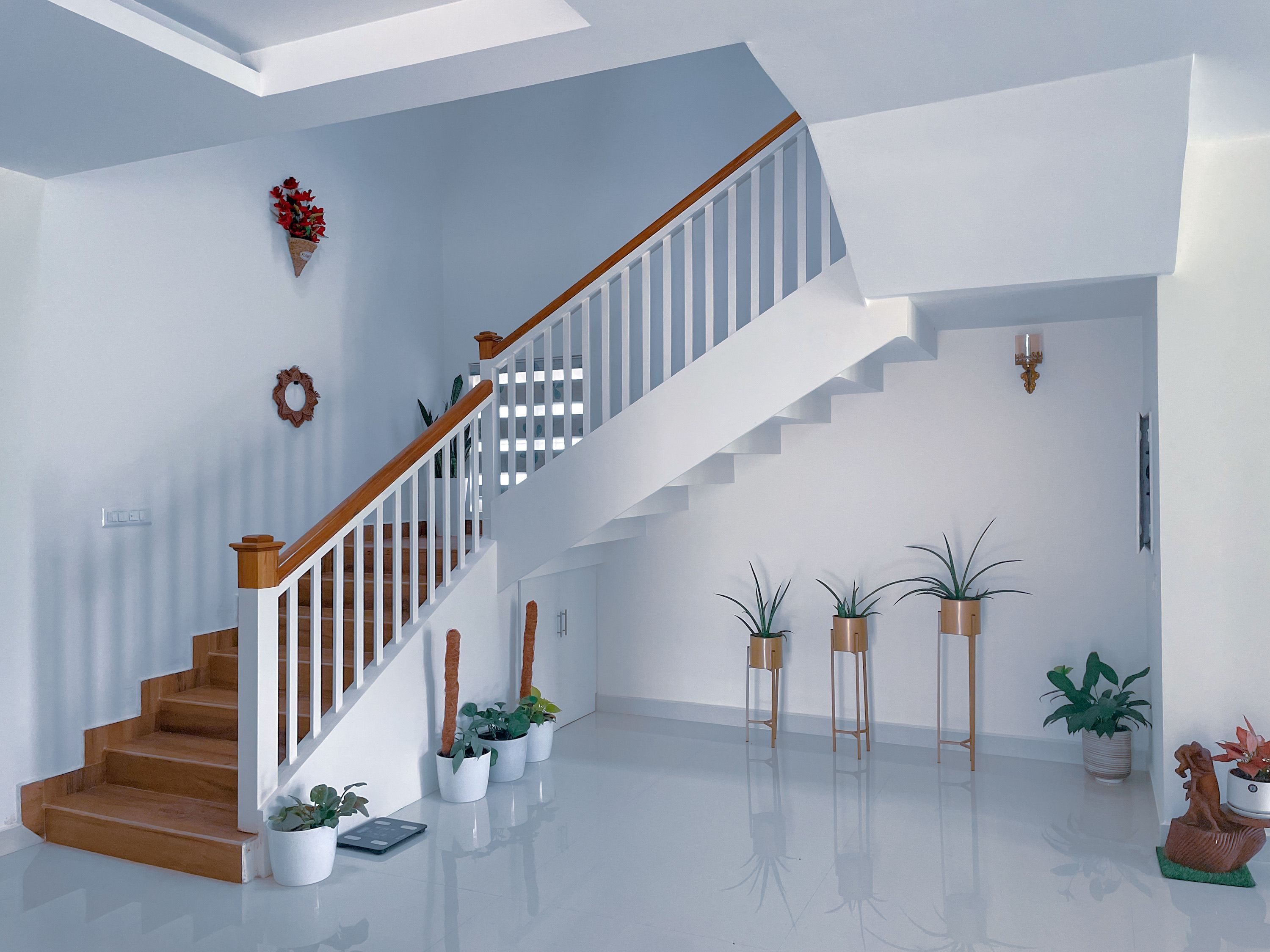 Corredor interno de uma casa com destaque para a escada de madeira e decoração com plantas