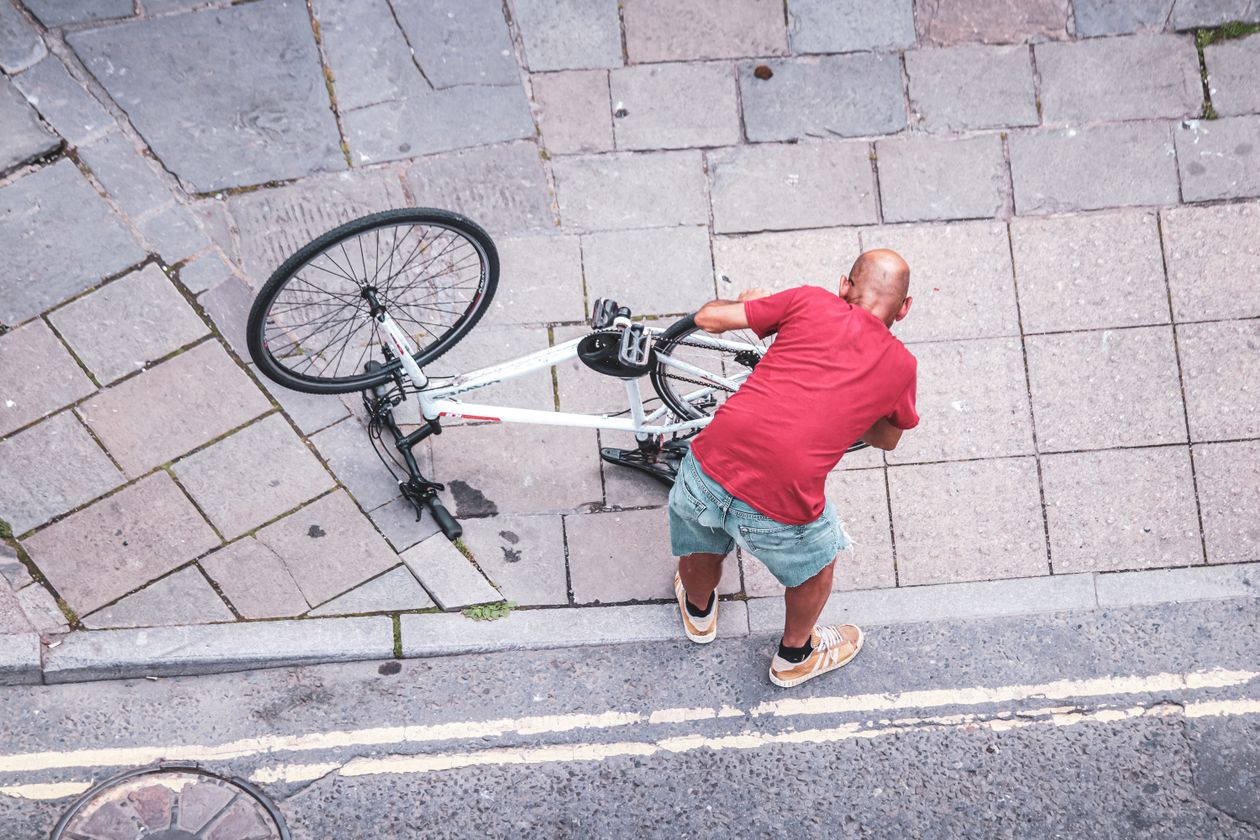 A man in a red shirt fixes his bicycle after a crash, illustrating why knowing when to contact a bicycle accident attorney matters.