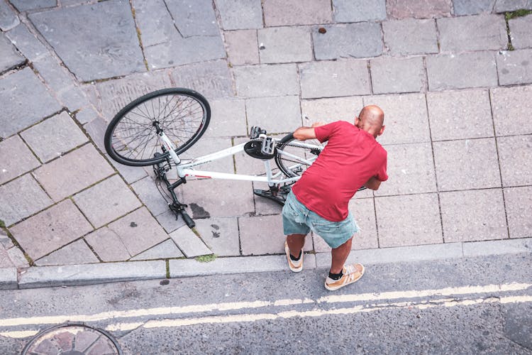 High Angle Shot Of Man In Red Shirt Fixing The Bike 