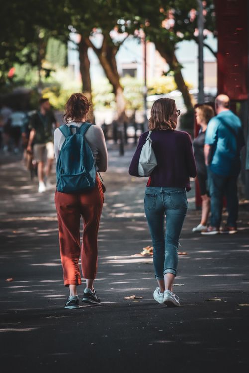 Free Two women with backpacks walk down a tree-lined street, enjoying a sunny day. Stock Photo