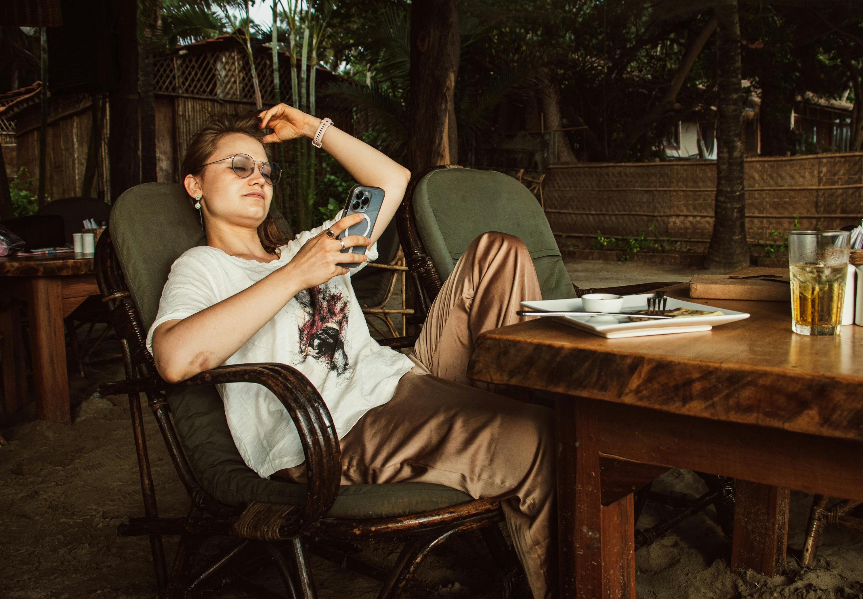 woman in white t shirt and brown pants sitting on brown armchair using phone