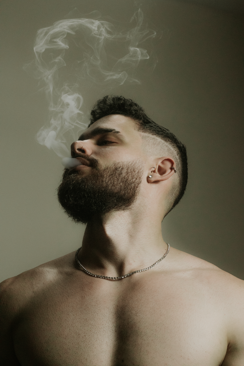 Free Close-up of a shirtless bearded man exhaling smoke in a moody, artistic setting. Stock Photo