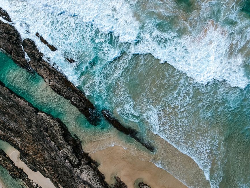 A breathtaking aerial view of waves crashing on Coolangatta Beach's rocky shore in Queensland, Australia.
