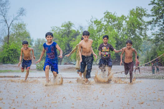 A group of boys playing joyfully in a muddy puddle during rain, showcasing friendship and fun outdoors.
