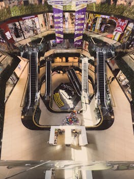 Top-down view of a bustling shopping mall with escalators and storefronts.
