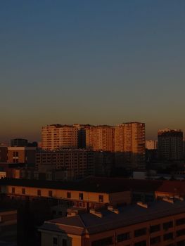 A serene urban skyline at sunset featuring high-rise buildings with a clear sky backdrop.