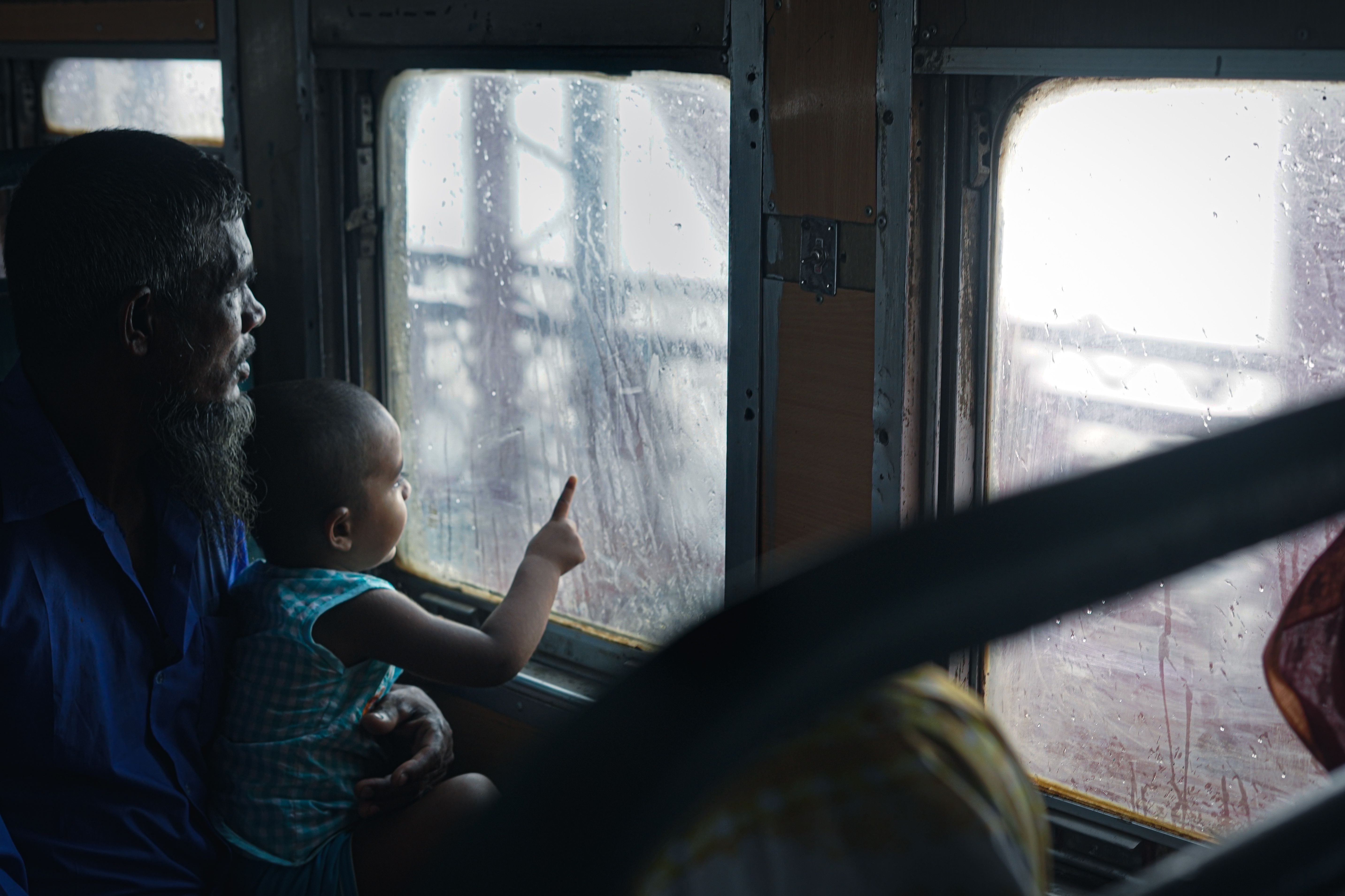A father and child gaze out a rainy bus window in Bangladesh, capturing a moment of travel and curiosity.