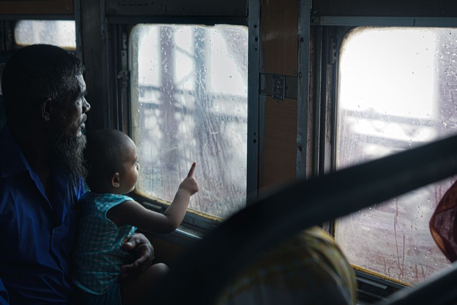 A father and child gaze out a rainy bus window in Bangladesh, capturing a moment of travel and curiosity.