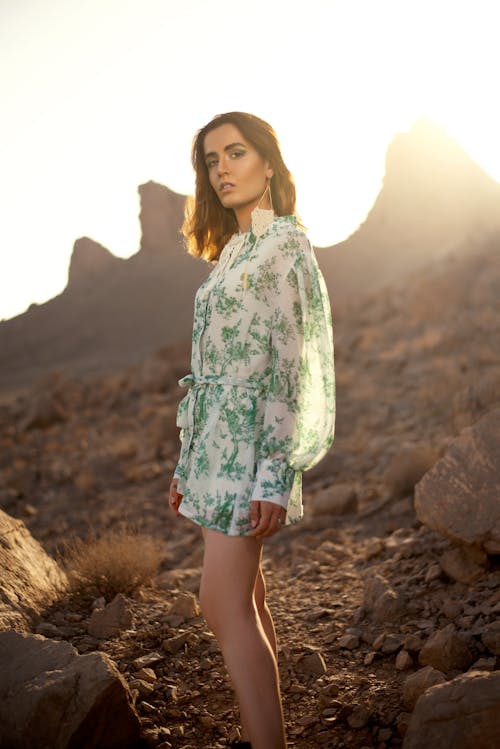 Free Woman in White Green and Blue Floral Dress Standing on Rocky Ground Stock Photo