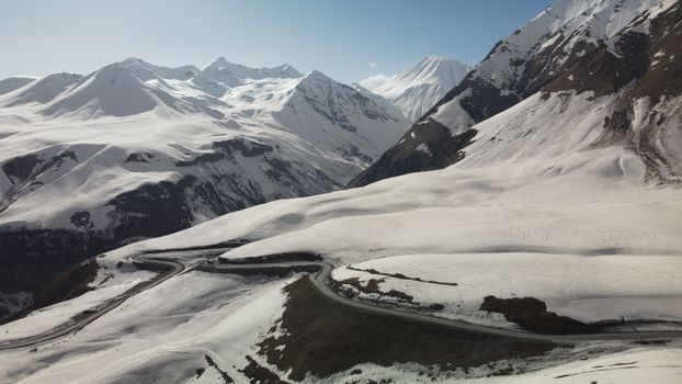 Aerial shot of winding road through snow-covered mountains under clear sky.