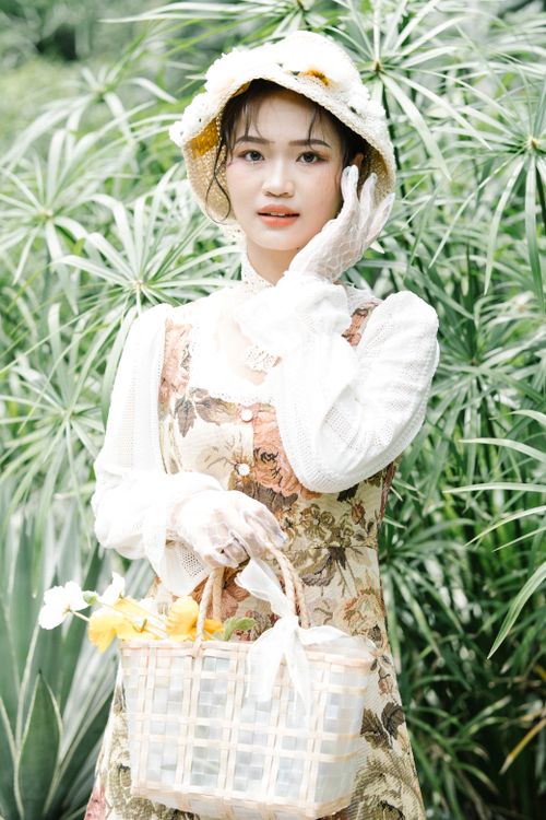 Free Elegant woman in floral dress with a basket amidst lush greenery, capturing a vintage garden vibe. Stock Photo