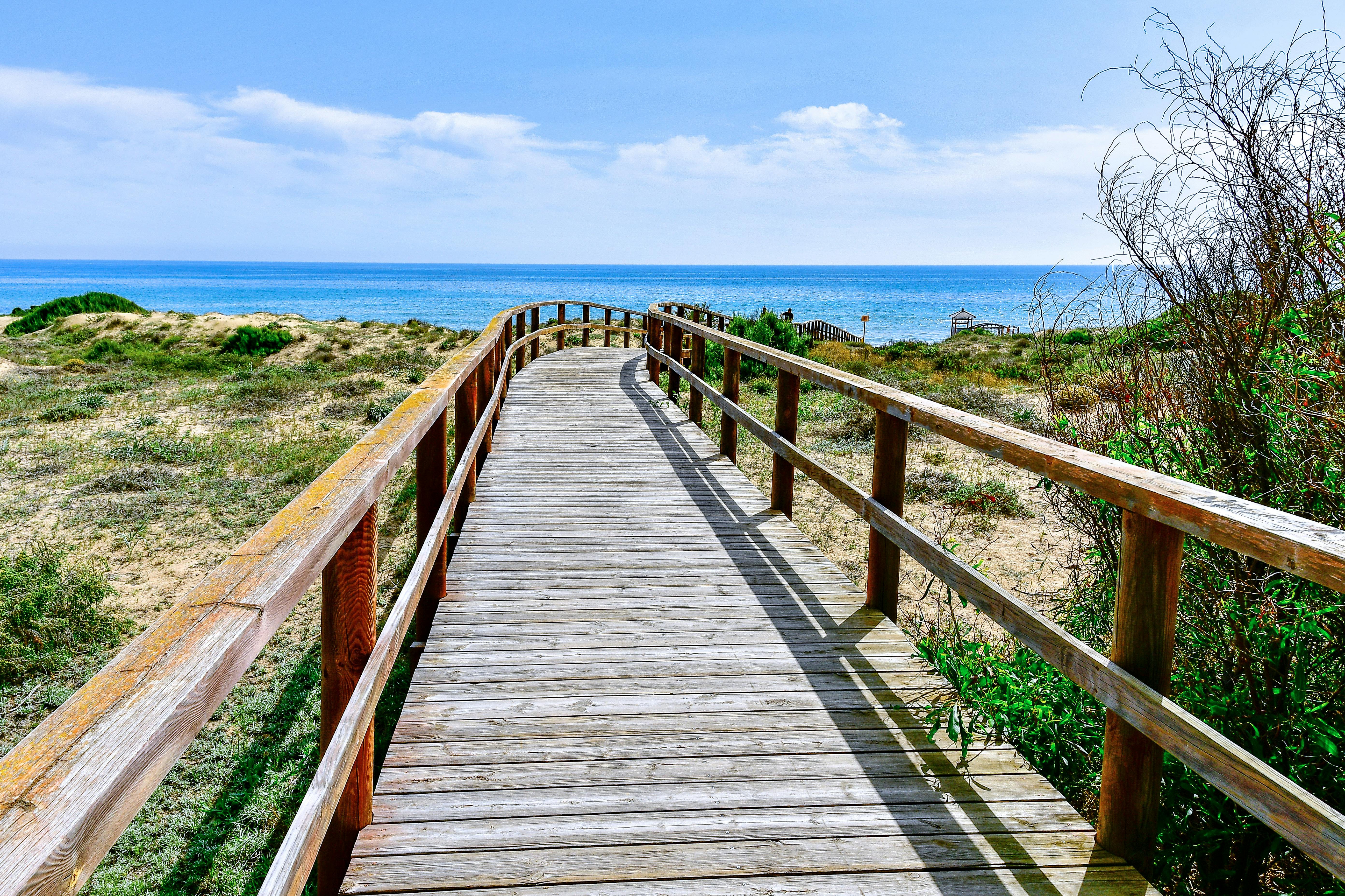 Explore the serene wooden pathway leading to the vibrant blue sea at Los Arenales del Sol, Spain.