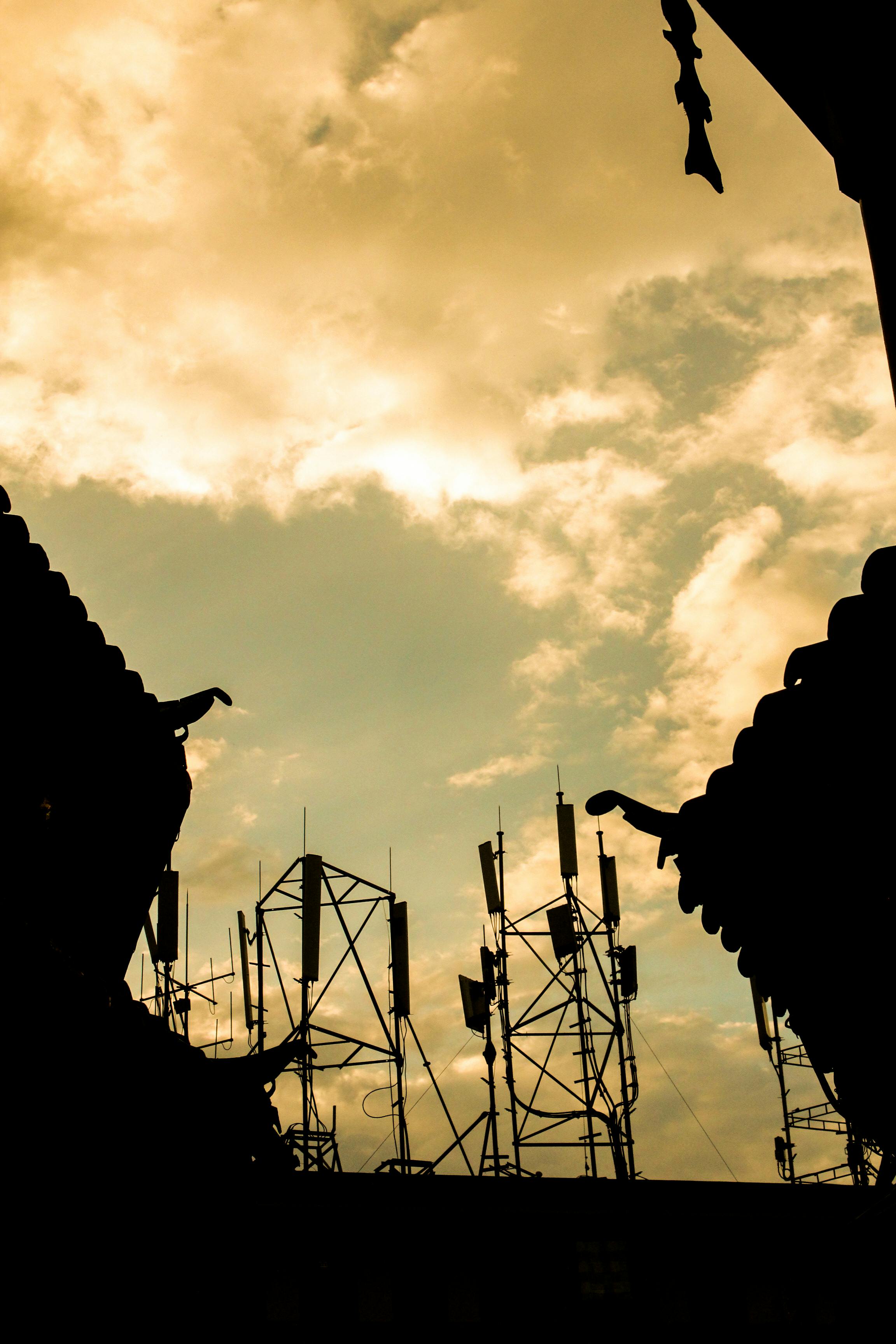 Silhouette of communication towers amidst traditional rooftops during a warm sunset in Lijiang, China.