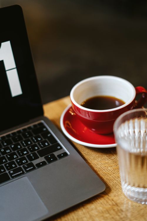 Free Enjoy a coffee and work session with a red cup, laptop, and glass of water. Stock Photo
