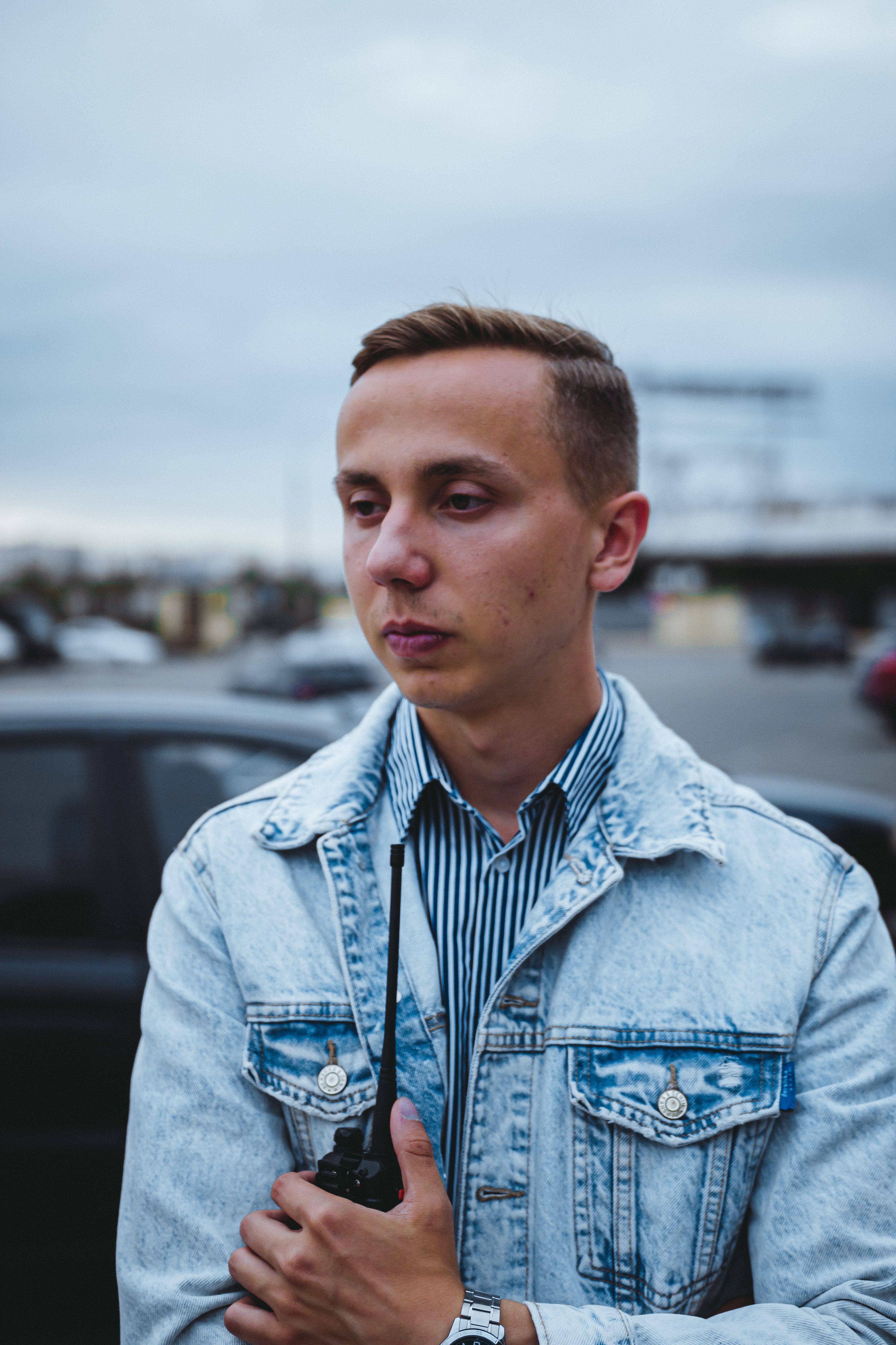 Portrait of a young man in a denim jacket holding a walkie-talkie, outdoors.