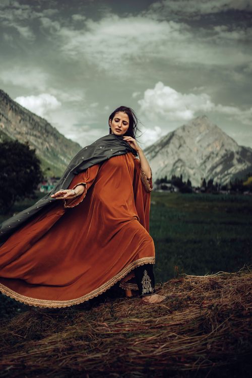 Free An Indian woman gracefully poses outdoors in an elegant traditional dress with a scenic mountain backdrop. Stock Photo