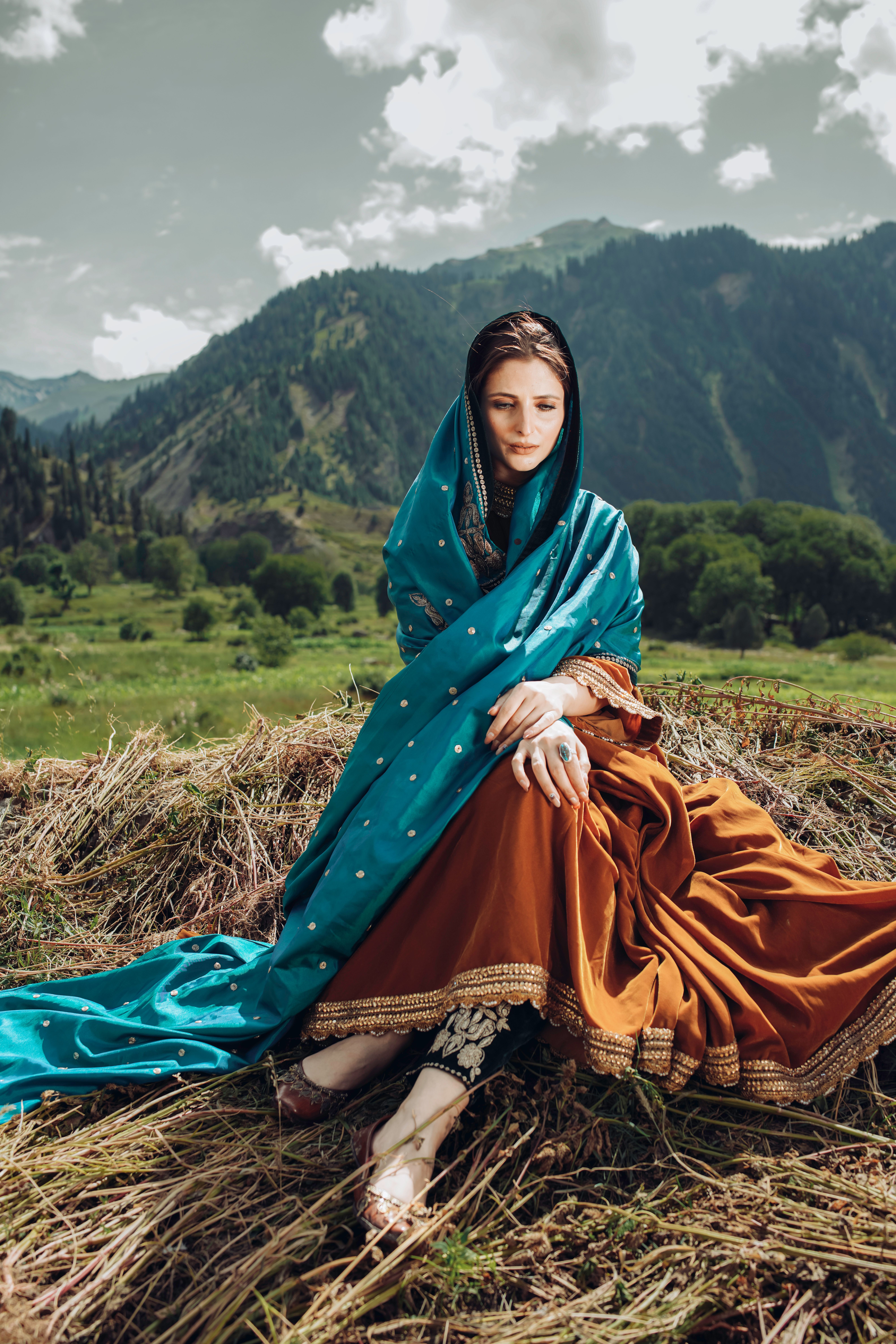 Woman in traditional attire sitting in a serene mountainous pasture.