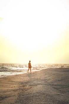 Peaceful sunset scene with person walking on beach by the ocean, creating a calm and tranquil atmosphere.