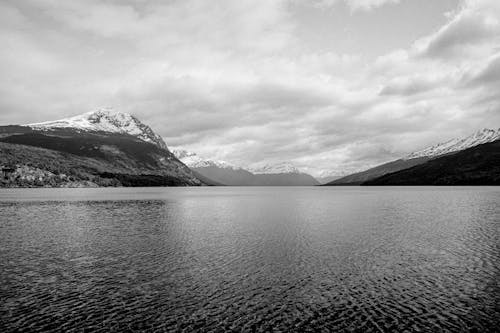 Grayscale Photo of Mountains near Lake under the Cloudy Sky