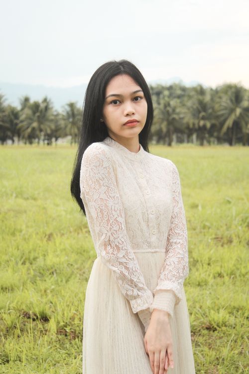 Free Portrait of a woman in a lace dress posing peacefully in a lush green field. Stock Photo