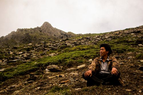 Free A man enjoying a peaceful moment sitting on rocky terrain at the base of a mountain. Stock Photo