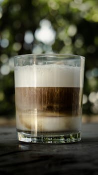 A refreshing latte macchiato in a clear glass with a blurred nature background, perfect for coffee lovers.