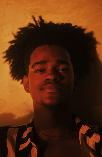 Warm-toned portrait of a smiling young person with afro hair in stylish lighting.