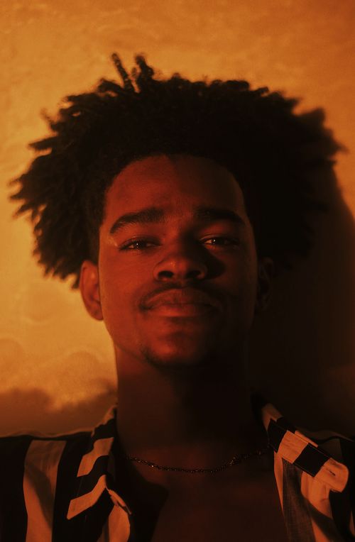 Free Warm-toned portrait of a smiling young person with afro hair in stylish lighting. Stock Photo