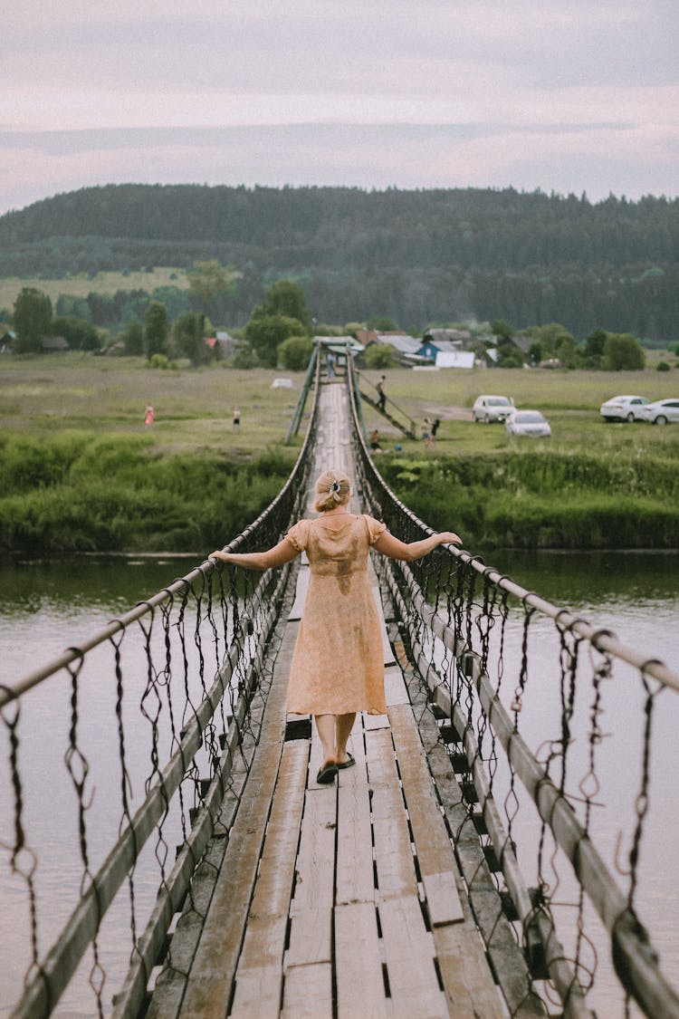 Woman Walking On A Hanging Suspension Bridge Over River 