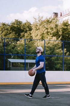Caucasian man carrying a basketball on an outdoor court during the day.