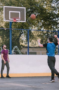 Two men playing basketball on an outdoor court on a sunny day.