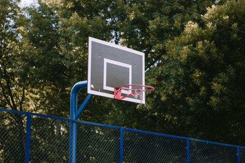 Free A basketball hoop on an outdoor court with lush green trees in the background. Stock Photo