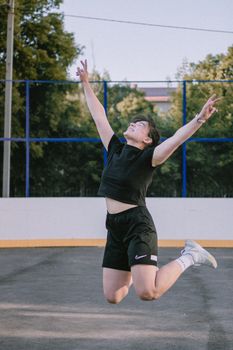 Young woman in black sportswear jumps mid-air smiling in an outdoor setting.