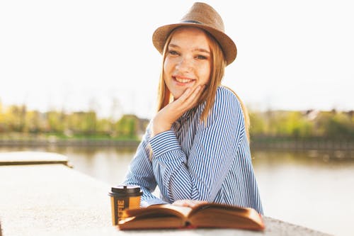 Woman Sitting While Holding Book Page Near Lake