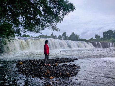Woman in red jacket standing by a cascading waterfall in Chi Phat, Cambodia.