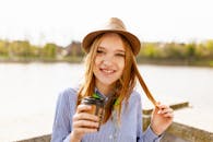 在一个阳光明媚的日子，一位愉快的女人戴着帽子在户外享受咖啡