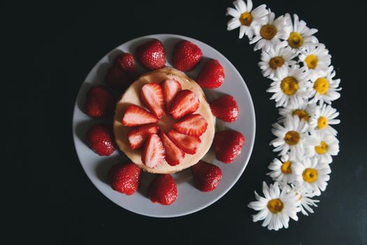 A top view of a delicious pancake adorned with fresh strawberries and surrounded by daisies.