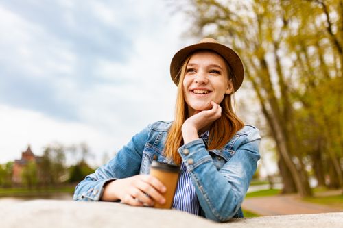 Free Casual woman in denim and hat enjoying a sunny day with coffee outdoors. Stock Photo