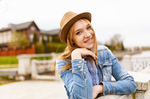 微笑的女人，穿着蓝色牛仔纽扣式外套和棕色的帽子，用手在她的脸上