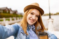 一位戴着软毡帽的年轻女子在湖边喝咖啡自拍