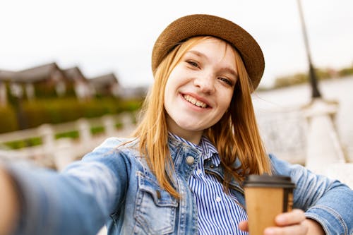 笑顔でコーヒーカップを保持している青いデニムジャケットの女性のセレクティブフォーカス写真