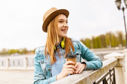 ベージュのコンクリートの手すりに寄りかかって茶色のカップを保持している女性