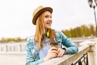 春日阳光明媚，一位微笑的年轻女子戴着帽子，穿着牛仔夹克，在户外喝咖啡