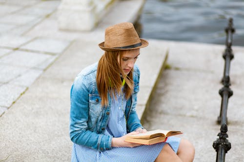 Woman Sitting on Grey Concrete Pavement Reading Book