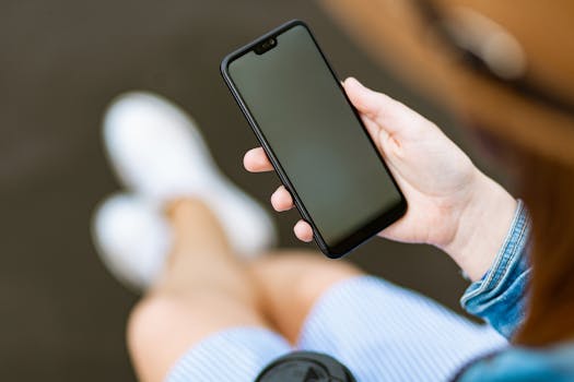 一位年轻女子随意地穿着牛仔夹克和条纹连衣裙，在户外拿着智能手机
